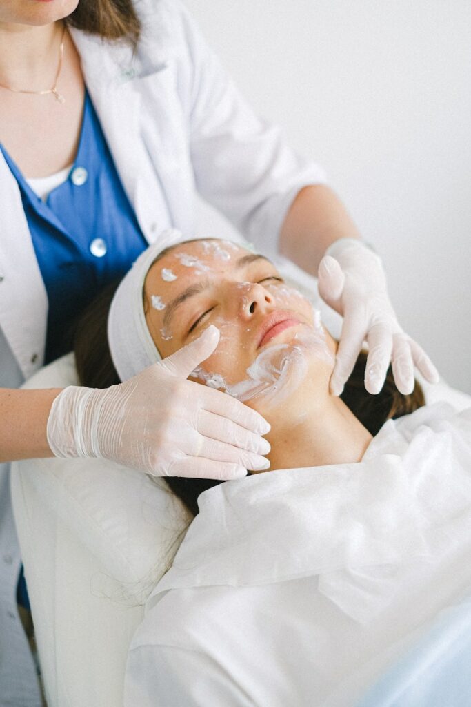 From above of crop faceless cosmetician applying facial mask on customer face during cosmetic procedure in modern spa salon